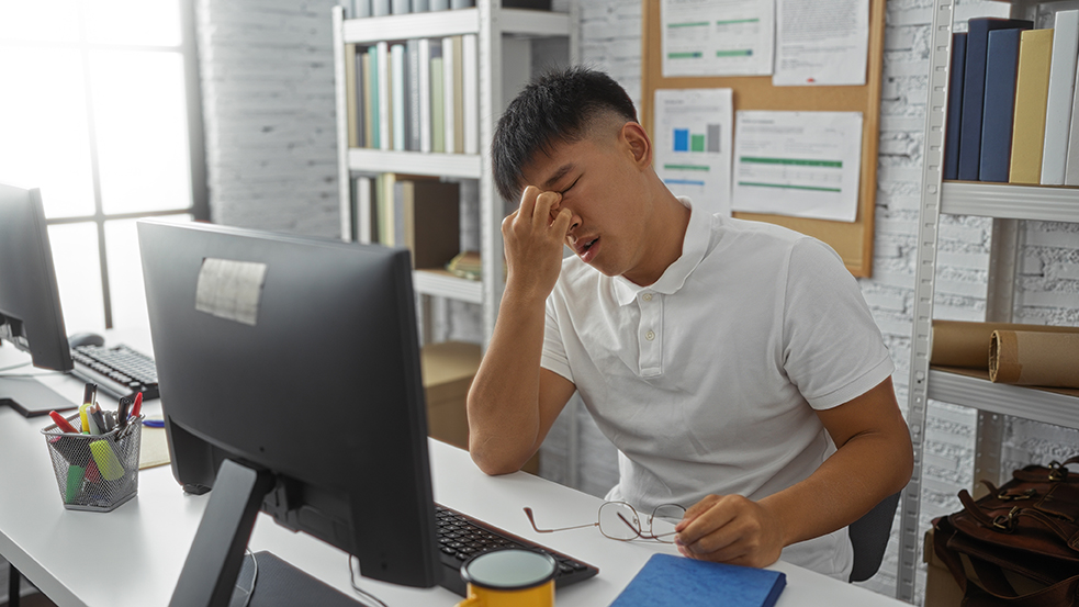 Man sitting down with eyes closed and hand on forehead, appearing exhausted and low in energy. 