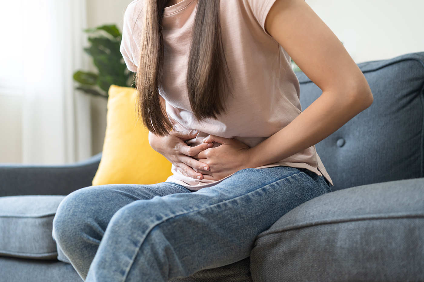 Woman holding her abdomen while sitting down and experiencing abdominal pain.